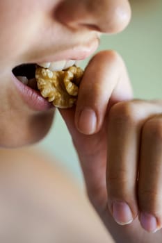 Closeup of crop unrecognizable teenage girl biting healthy walnut kernel at home