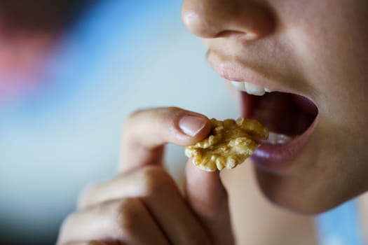 Closeup of crop unrecognizable young girl with mouth open about to eat healthy walnut at home