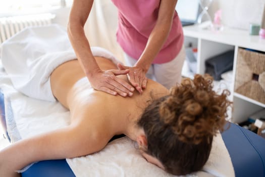 High angle of crop anonymous female massage therapist massaging back using professional technique during physiotherapy session in light clinic room