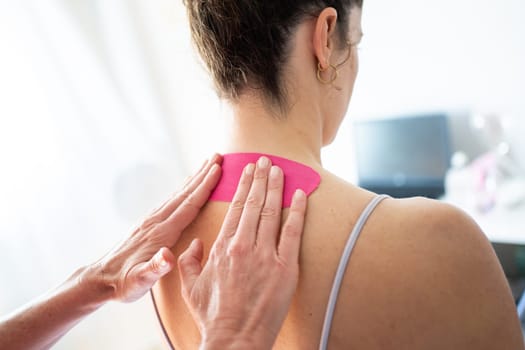 Back view of crop anonymous female therapist applying kinesiology tape on back of female patient during physiological massage in modern clinic