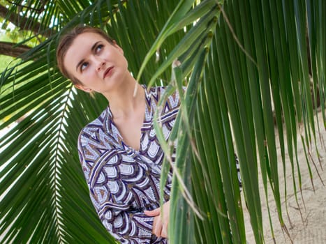 Beautiful young woman standing near palm leaves at sea