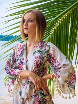 Beautiful young woman standing near palm leaves at sea