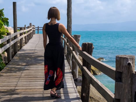 A girl stands on a wooden pier and looks at the sea