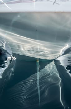 the stern of the sailboat and the rudder feather in the azure water, sun reflections are on glossy board of moored sail boat, Monaco, Monte-Carlo, tranquillity in port Hercules at sunny day. High quality photo