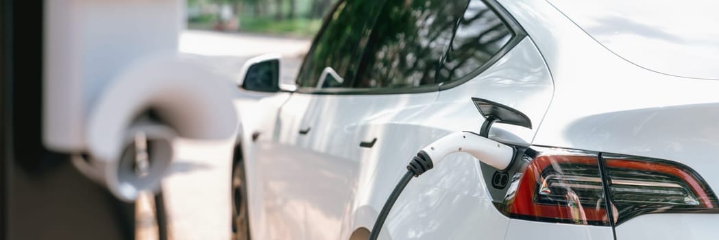 Panorama banner EV electric vehicle recharging battery from EV charging station in national park or outdoor forest scenic. Natural protection with eco friendly EV car travel in the summer woods. Exalt