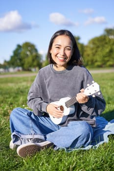 Positive hipster asian girl, playing ukulele and making faces, singing and feeling happy.