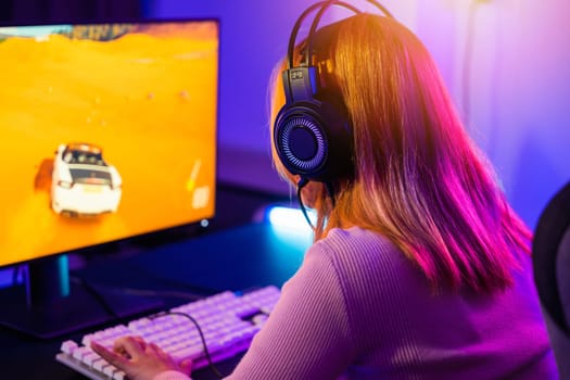 Young player woman wearing gaming headphones intend to do playing live stream games online at home, Happy Gamer endeavor plays online video games tournament with computer with neon lights, Back view