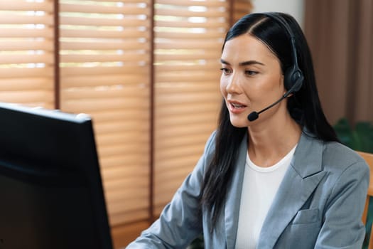 Female call center operator or customer service helpdesk staff working on workspace while talking on the headset to provide assistance for customer. Professional modern business service. Blithe