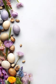 Assortment of speckled eggs and spring flowers on white background.