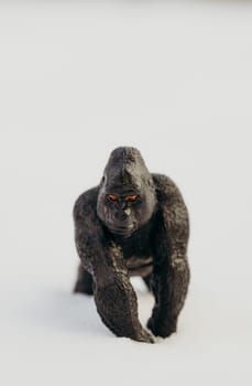 One small toy black gorilla with red eyes stands angrily in the snow with copy space from above on a winter day, side view close-up.