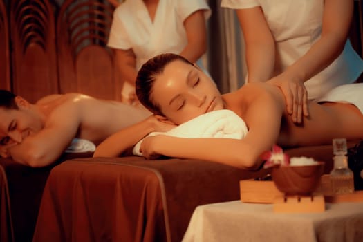 Caucasian couple customer enjoying relaxing anti-stress spa massage and pampering with beauty skin recreation leisure in warm candle lighting ambient salon spa at luxury resort or hotel. Quiescent