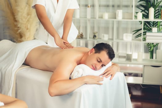 Caucasian couple customer enjoying relaxing anti-stress spa massage and pampering with beauty skin recreation leisure in day light ambient salon spa at luxury resort or hotel. Quiescent