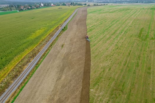 A tractor plows a field sown with green manure near a railway in a hilly area. Season of work in the farmer's field.