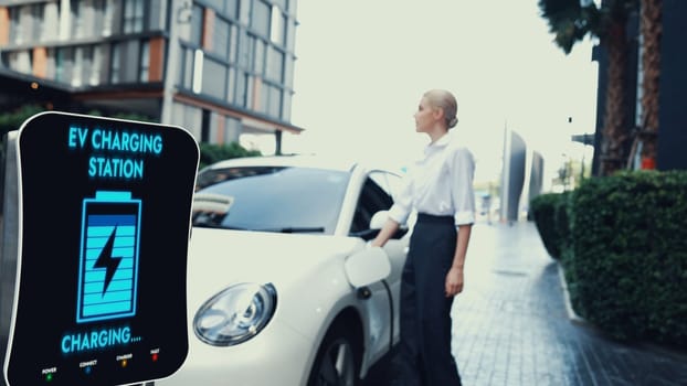 Businesswoman recharge her electric car from charging station at city center or public parking car. Eco friendly rechargeable car using alternative clean energy. Peruse