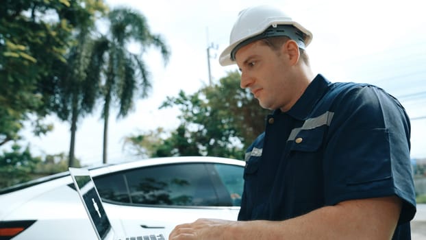 Qualified technician working on home EV charging station installation, making troubleshooting and configuration setup on charging system with empty laptop screem for EV at home. Synchronos