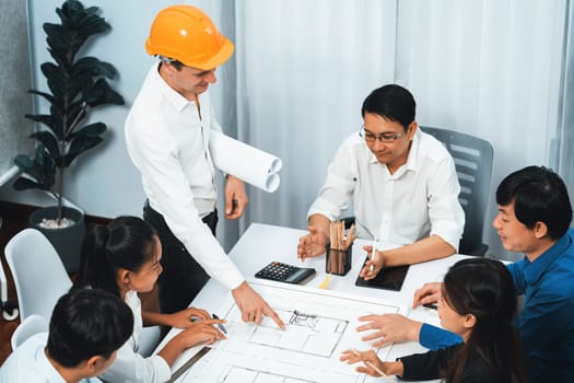 Diverse group of civil engineer and client working together on architectural project, reviewing construction plan and building blueprint at meeting table. Prudent