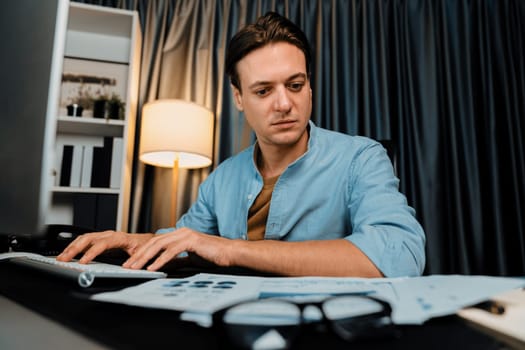 Smart businessman typing with keyboard on monitor with business paragraph dynamic data marketing analysis planning sheet aligning on report paperwork at modern home office at night time. Pecuniary.