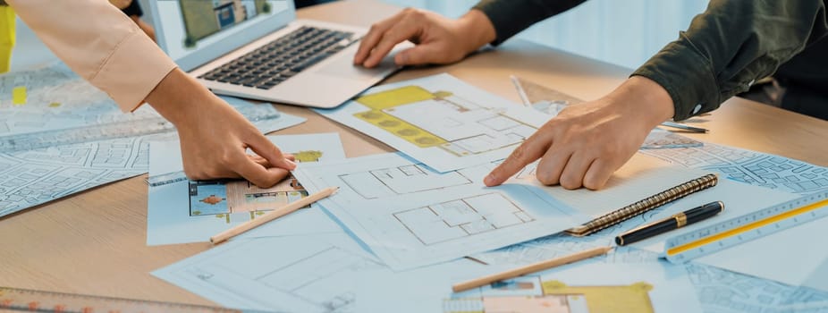 Professional architect shows mistake structure in blueprint while analysis and comparison with picture in laptop on table with blueprint and architectural equipment. Cropped image. Delineation.
