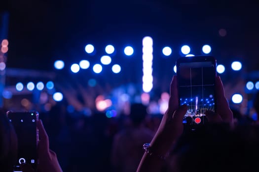 A lively concert festival at night with a cheering unrecognizable crowd in front of the brilliantly lit stage. The lens flare adds to the excitement as people have a blast during this music event.