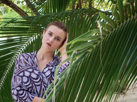 Beautiful young woman in bikini standing near palm leaves
