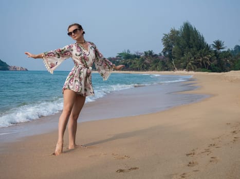 young beautiful girl in glasses dancing on the sand by the tropical sea