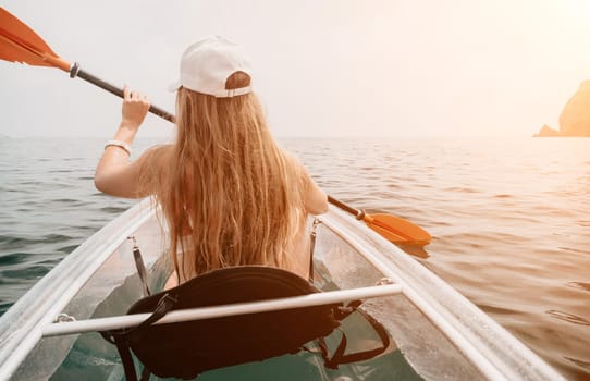 Woman in kayak back view. Happy young woman with long hair floating in transparent kayak on the crystal clear sea. Summer holiday vacation and cheerful female people having fun on the boat.