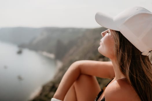 Woman travel sea. Happy tourist taking picture outdoors for memories. Woman traveler looks at the edge of the cliff on the sea bay of mountains, sharing travel adventure journey.