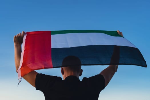 Man holding National Flag Of UAE Waving In The Wind sunset. Flag of United Arab Emirates on Sun Background. Sign of Dubai. Spirit of the Union National Independence Day or Flag day