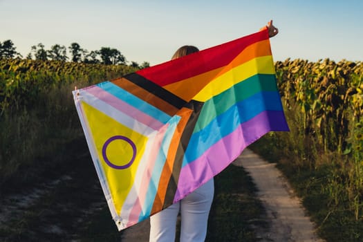 Young woman run in field with Rainbow LGBTQIA flag waving in wind made from silk material on field background. Symbol of LGBTQ pride month. Equal rights. Peace and freedom concept