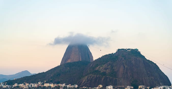 A serene view of Sugarloaf Mountain with cloud cover at sunset, overlooking Rio de Janeiro