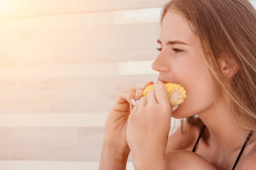 Healthy vegetarian hipster woman in summer outfit eat grilled corn and look to camera. Sexy lady on sea beach sunset or ocean sunrise. Travel, explore, active yoga and meditation lifestyle concept.