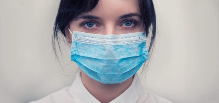 Portrait of a young European woman in a protective disposable medical mask. Concept of caronavirus Cavid 19 and human quarantine. Girl in a mask on a white wall. Masked medical worker