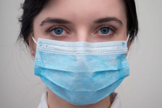 Portrait of a young European woman in a protective disposable medical mask. Concept of caronavirus Cavid 19 and human quarantine. Girl in a mask on a white wall. Masked medical worker