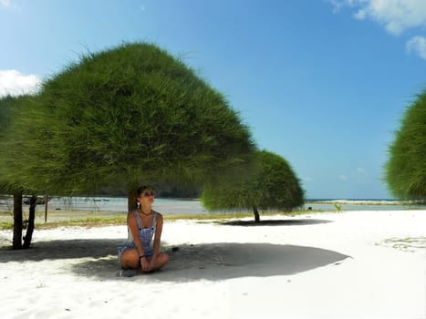 Young woman sit on the sand on a tropical sandy beach in the shade of trees. Malibu Beach, Koh Phangan, Thailand.