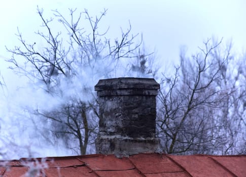 White smoke from the chimney of an old house during frost. Fireplace chimney on an iron roof.