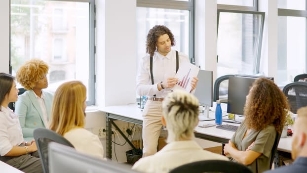 Photo of young man using graphics while talking in a coworking meeting