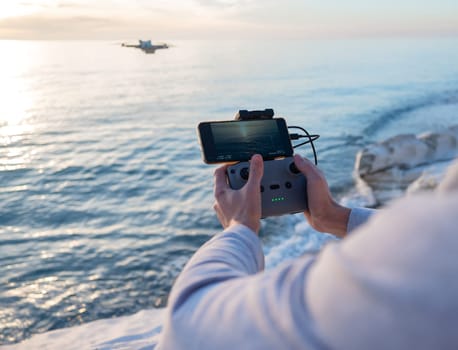 the remote control from the drone is in the hands of a man and the quadcopter is in flight against the background of sea