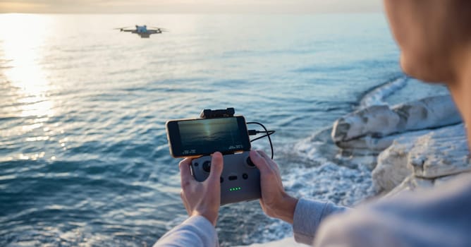 the remote control from the drone is in the hands of a man and the quadcopter is in flight against the background of sea