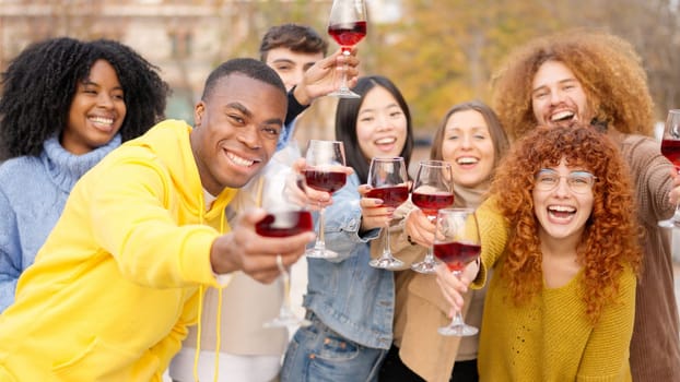 Group of multi-ethnic friends toasting with wine smiling at the camera outdoors
