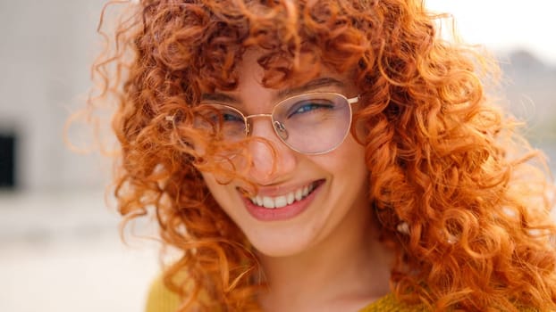 Young and redhead woman with curly long hair smiling at camera. Close up