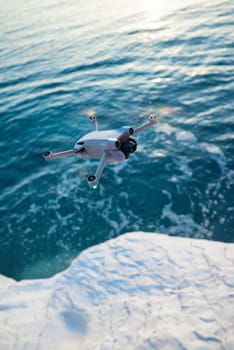 A quadcopter in flight against the background of a beautiful sea and white cliffs in sunset light