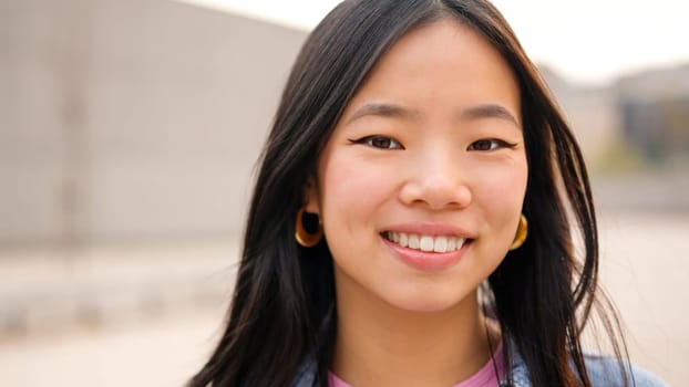 Asian young woman smiling at camera in the street. Close up