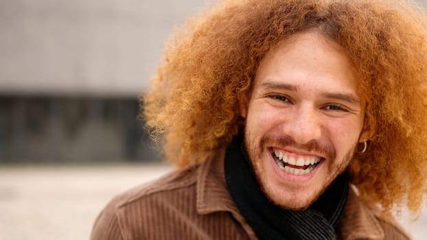 Alternative young man with curly hair laughing at camera. Close up
