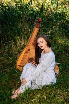 A Ukrainian woman with a bandura is sitting in the tall grass.