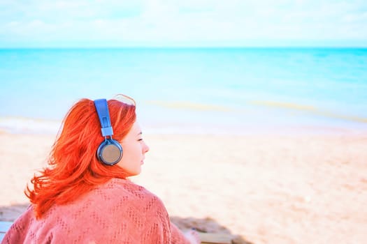 Cute redhead woman with headphones listening to music on the beach.