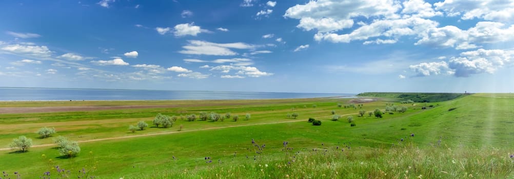 Green field and blue sky. Beautiful bright colorful summer spring landscape of green hills and sea. Panorama