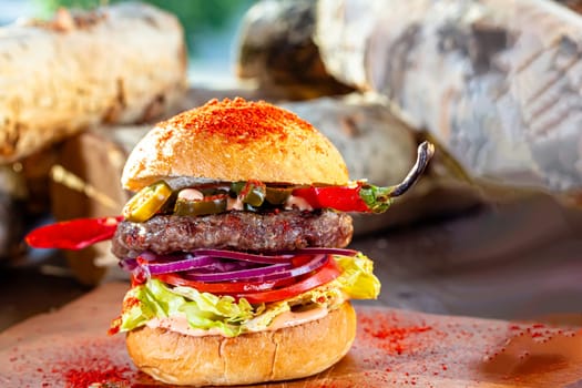 Hot chilli pepper cheeseburger with spicy chili sauce, a beef patty and melted cheese served with a side dish of crispy French Fries on a wooden board in rustic restaurant.