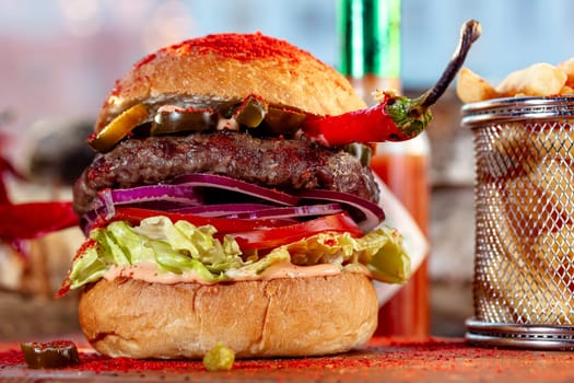 Hot chilli pepper cheeseburger with spicy chili sauce, a beef patty and melted cheese served with a side dish of crispy French Fries on a wooden board in rustic restaurant.