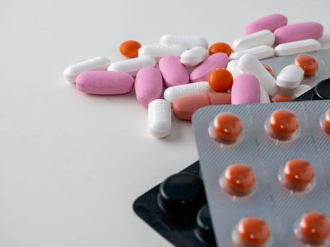 multicolored medical pills and packs of pills on a white table.