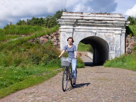 A woman is riding a blue bicycle with a basket of paving stones.